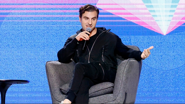 Airbnb CEO'su Brian Chesky, mavi arka planla sahnede gri sandalyede oturuyor