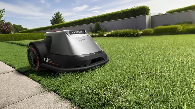 Eufy E18 Taş yolun yanındaki yeşil çimlerde çim biçme makineleri.