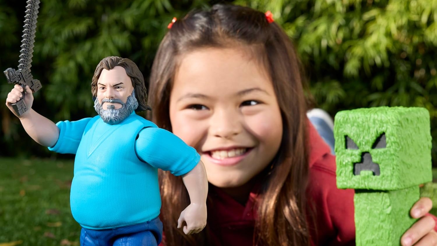 Genç bir kız her elinde bir oyuncak oynar ve tutar, biri Jack Black aksiyon figürü, diğeri Minecraft'tan yeşil bir sarmaşıktır