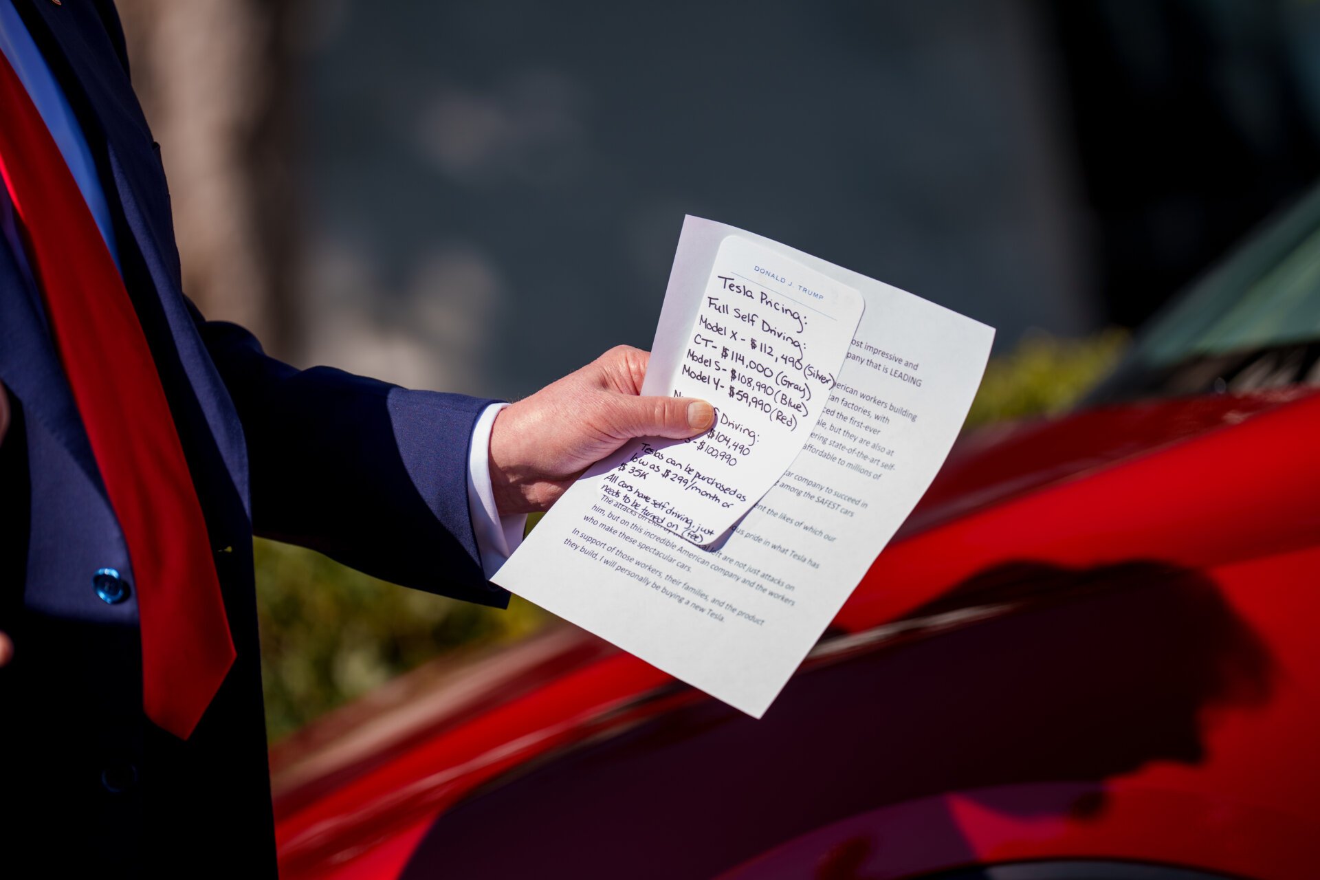 Donald Trump, 11 Mart 2025'te Washington DC'de Beyaz Saray'ın güney çimlerinde açıklamalar sunarken Tesla araçlarının fiyatlandırması hakkında notlar alıyor.