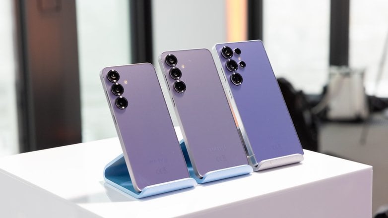 Zarif mor tasarımlarını gösteren bir stand üzerinde üç Samsung Galaxy S25 akıllı telefon.