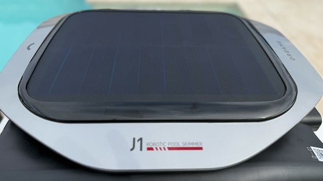 Yüzme havuzunun yakınında, üstte bir güneş paneli ile J1 Robot Havuz Skimmer'ı hayal edin.