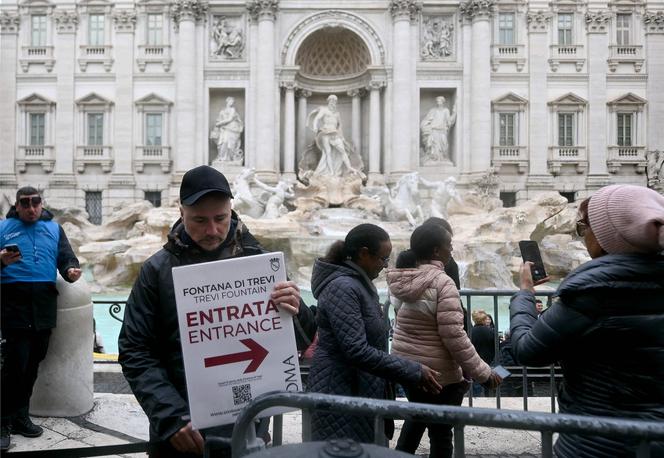 Un homme tient une pancarte sur laquelle est inscrit « Entrée » devant la fontaine de Trevi, à Rome, le 19 décembre 2025.