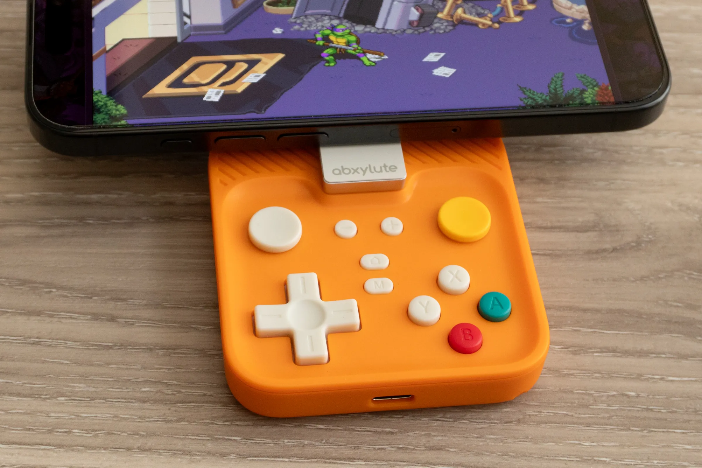 Abxylute M4 kontrol cihazı, iPhone 16 Pro ile bağlı, TMNT oyunu oynarken.