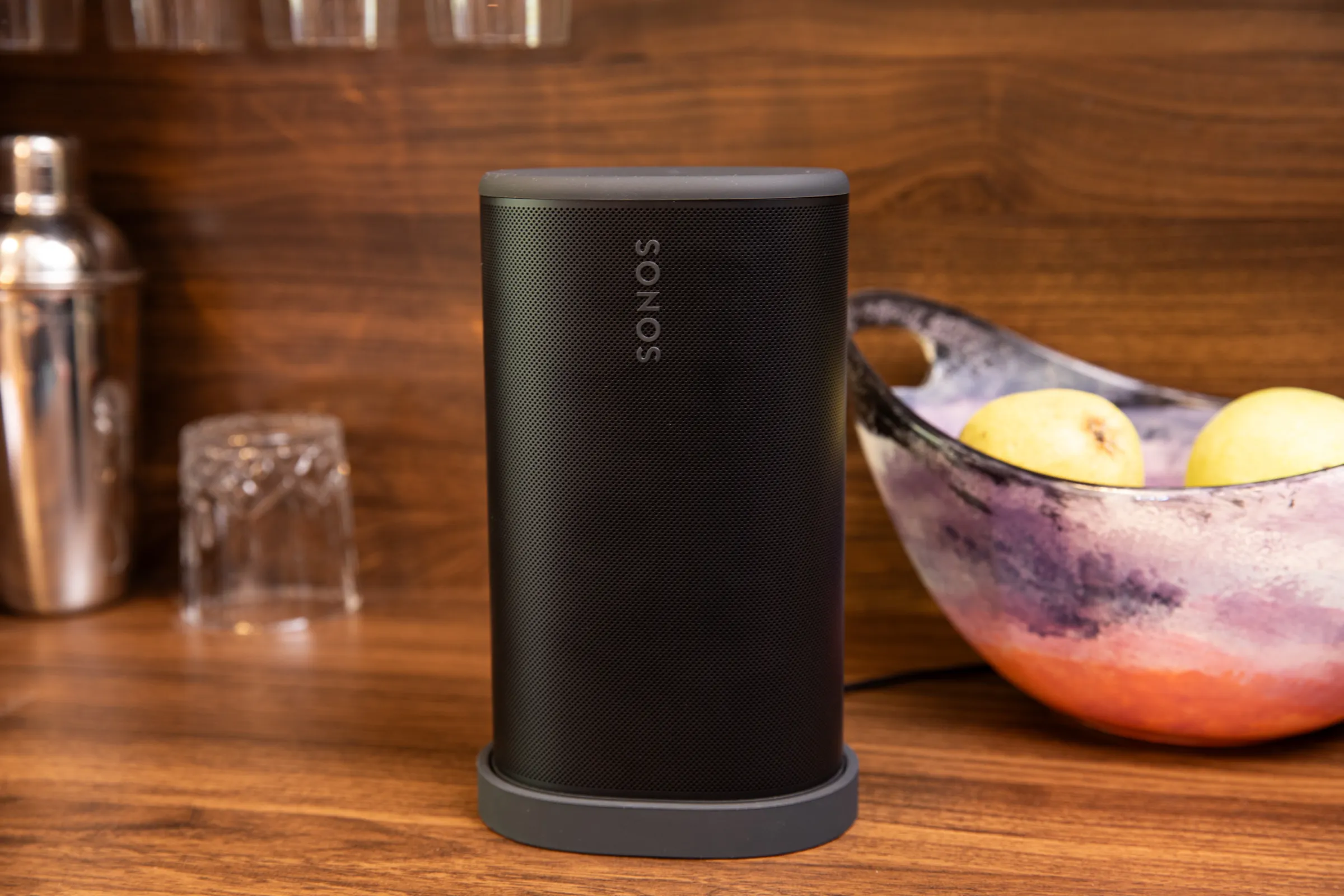 Sonos Play hoparlörü, şarj istasyonunda, arka planda meyve ve kokteyl malzemeleri.
