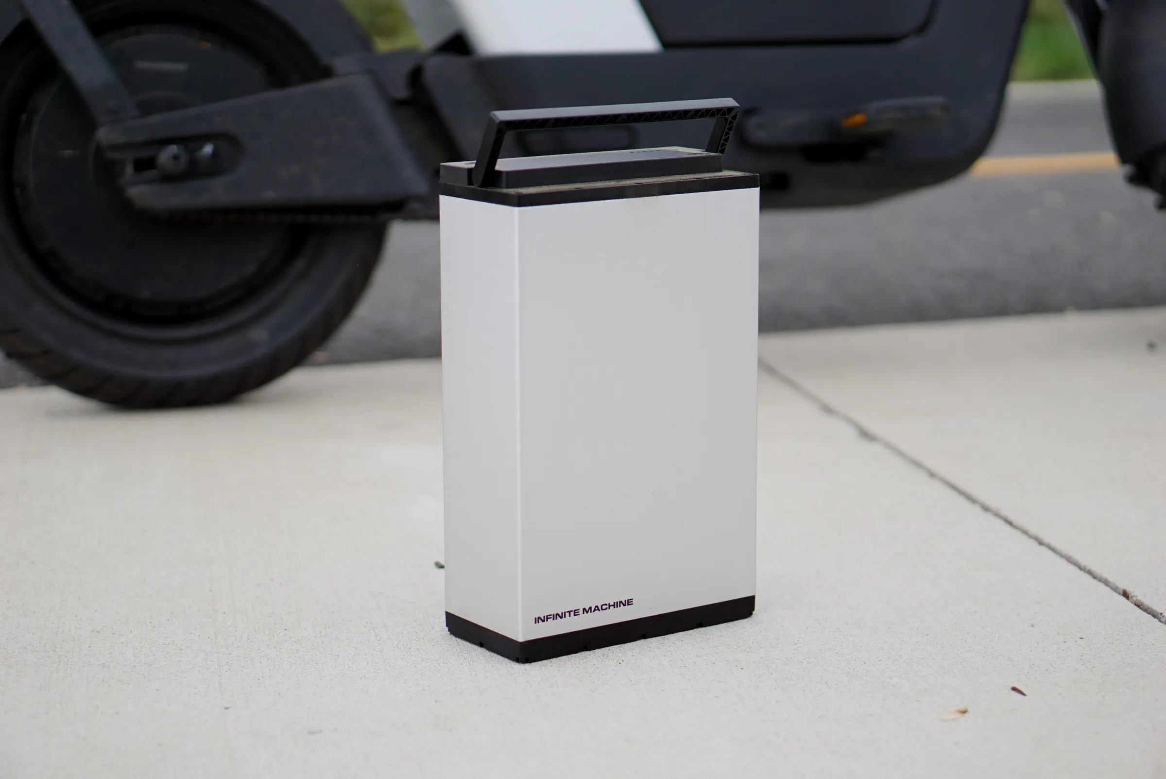A photo of a large silver battery, on the ground in front of a bike.