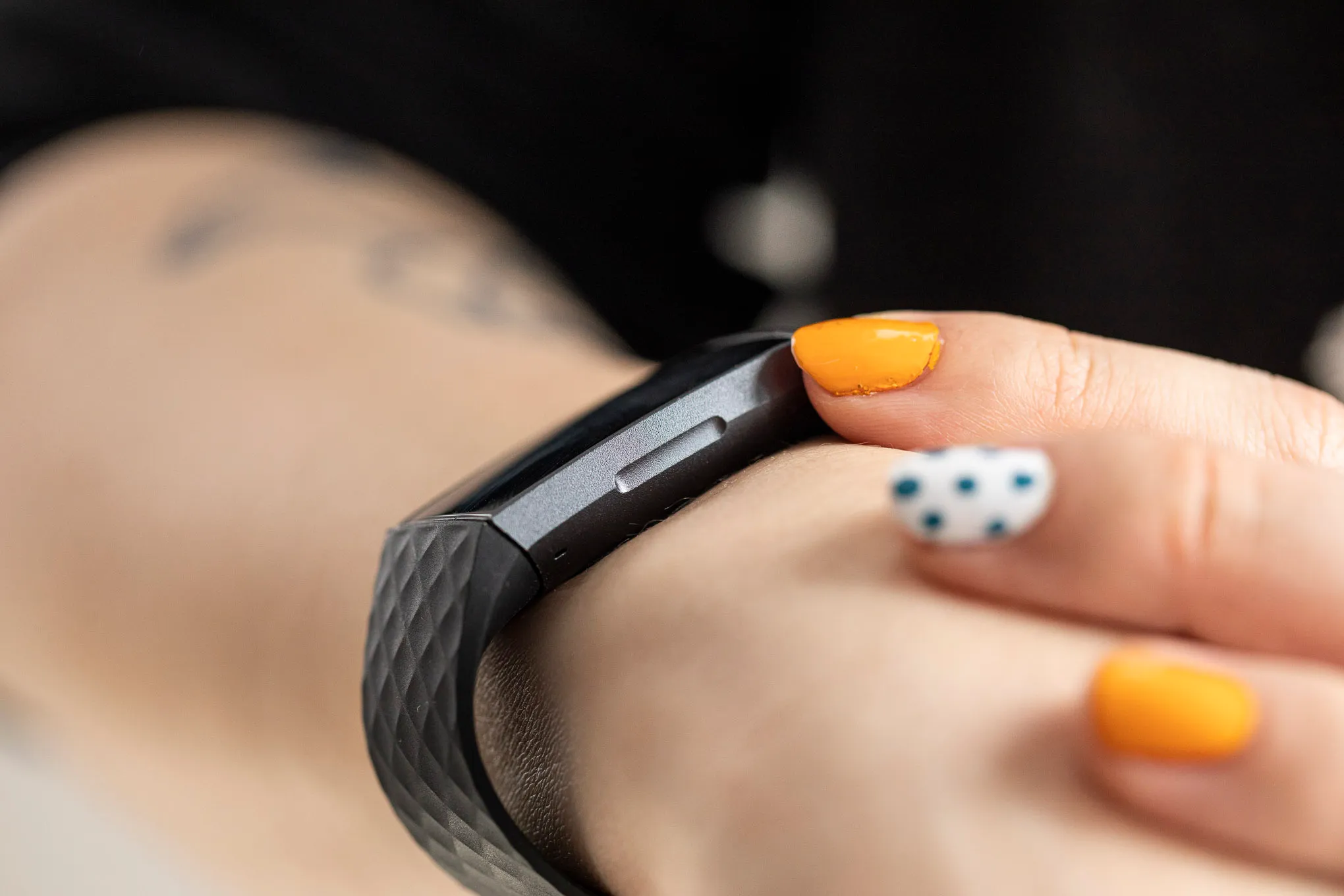Renkli oje takan bir kişinin, Fitbit Charge 3'ü kullanırken indüktif butonun açık bir görünümü.