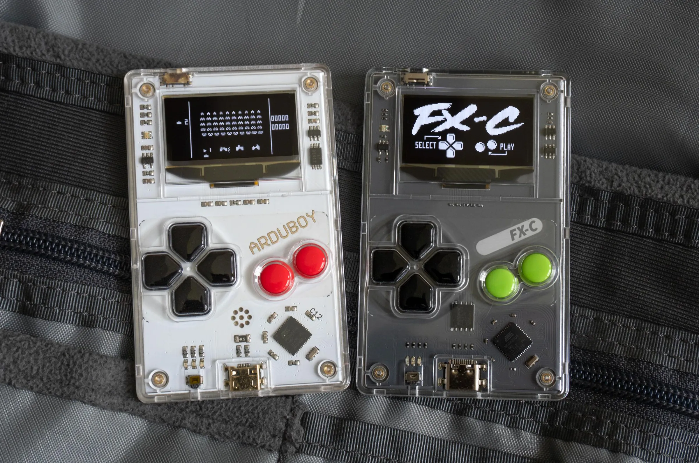 The original Arduboy next to the new Arduboy FX-C sitting on a backpack’s internal pockets.