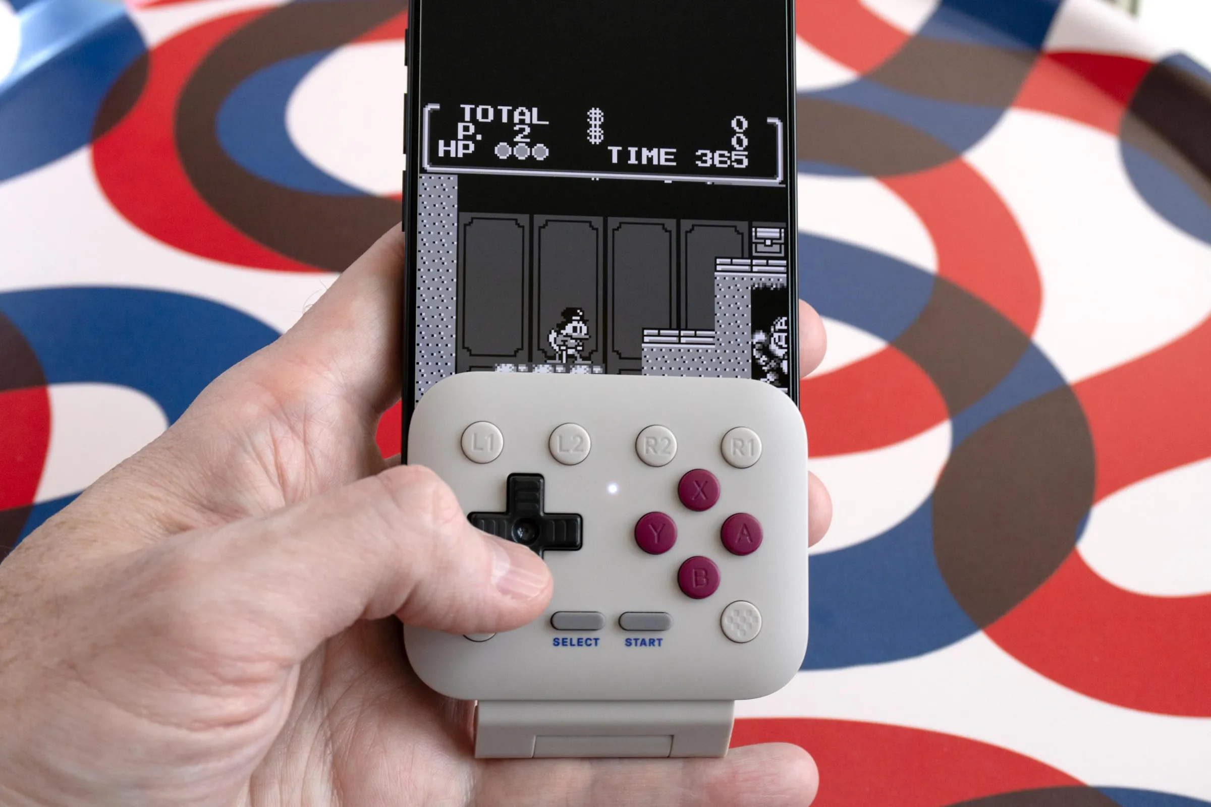 Bir kişi, iPhone'a takılı 8BitDo FlipPad ile Game Boy oyunu oynuyor.